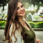 A cheerful woman with red lips and long hair enjoys a sunny day in an Ibarra park.